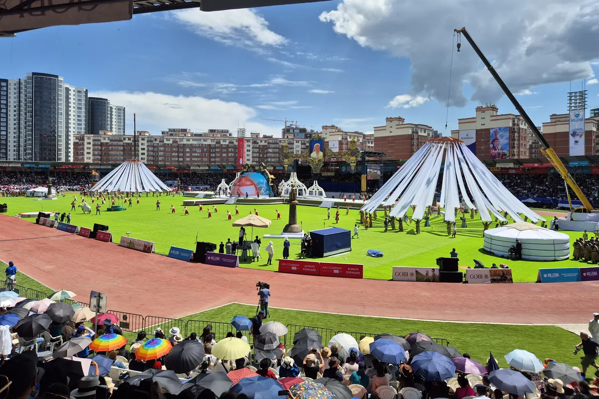 The Naadam opening ceremony at the National Sports Stadium in Ulaanbaatar, with white-ribboned canopies on the green field and spectators under umbrellas